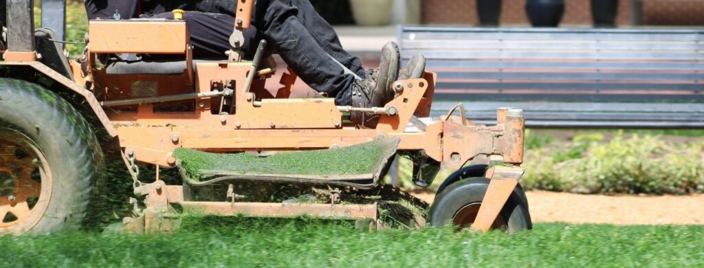 A landscaper mowing grass outside of a commercial building.